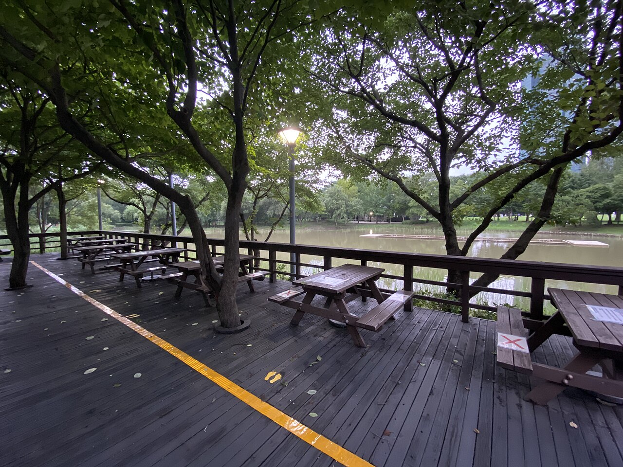 A wooden boardwalk and tables beside a pond surrounded by trees in Seoul Forest.